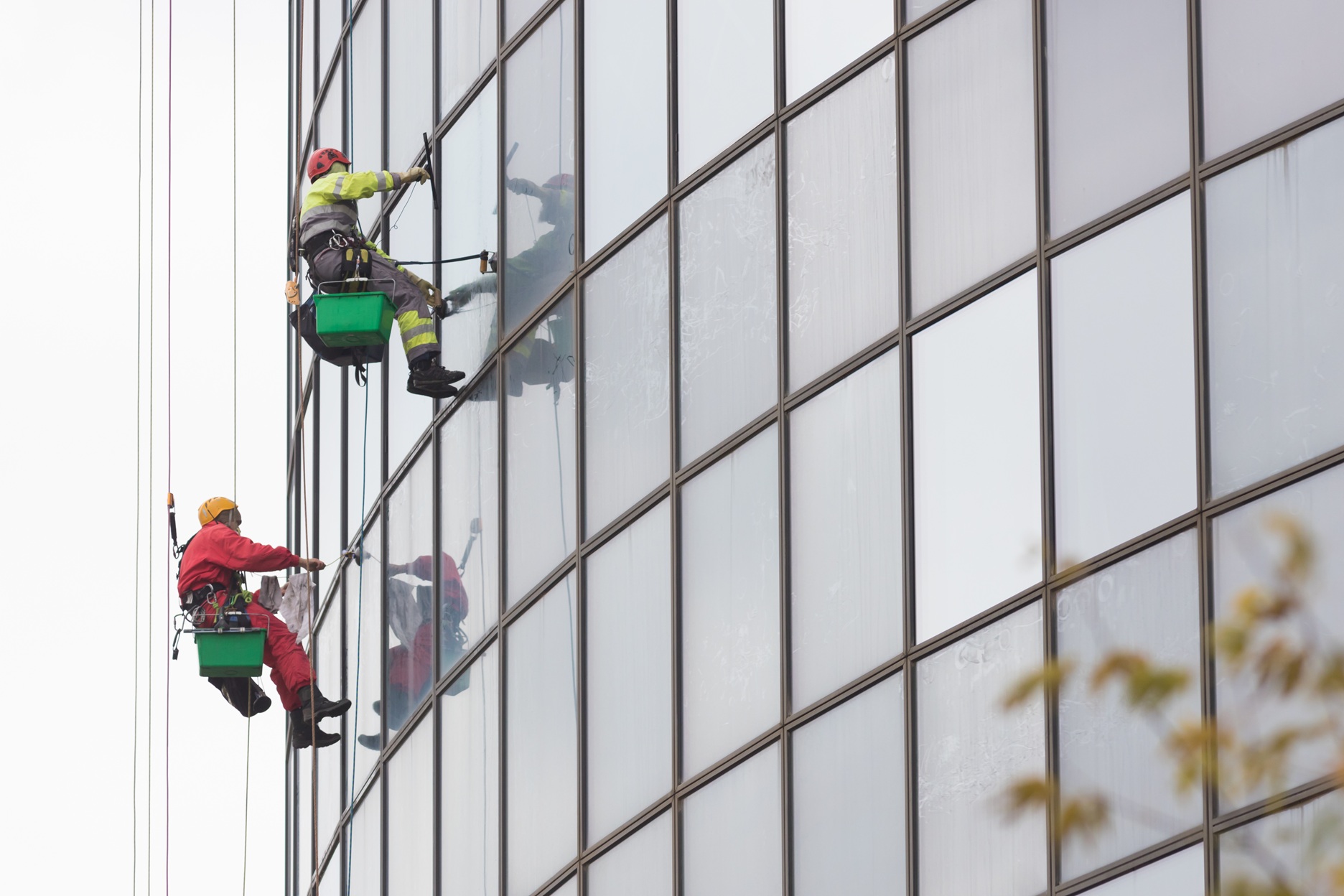 Dois homens limpando fachada de prédio suspensos com equipamento de segurança em altura.